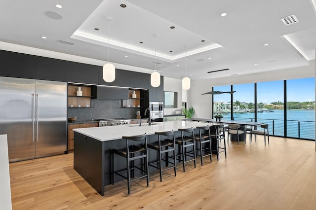 kitchen featuring pendant lighting, a water view, a tray ceiling, and built in refrigerator