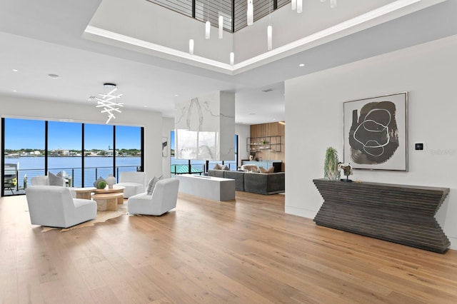 living room featuring a chandelier, a towering ceiling, a water view, and light hardwood / wood-style flooring