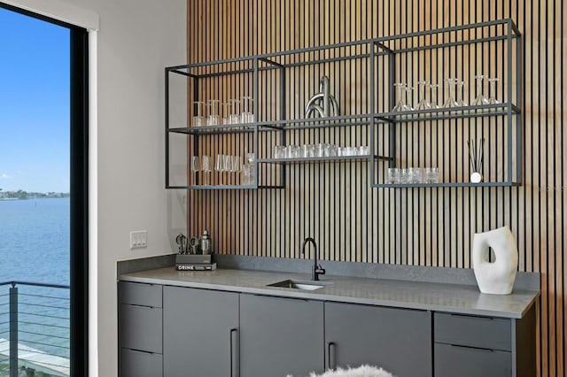 bar with a water view, gray cabinetry, and sink