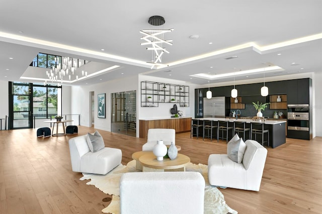 interior space featuring expansive windows, a tray ceiling, sink, light hardwood / wood-style flooring, and a chandelier