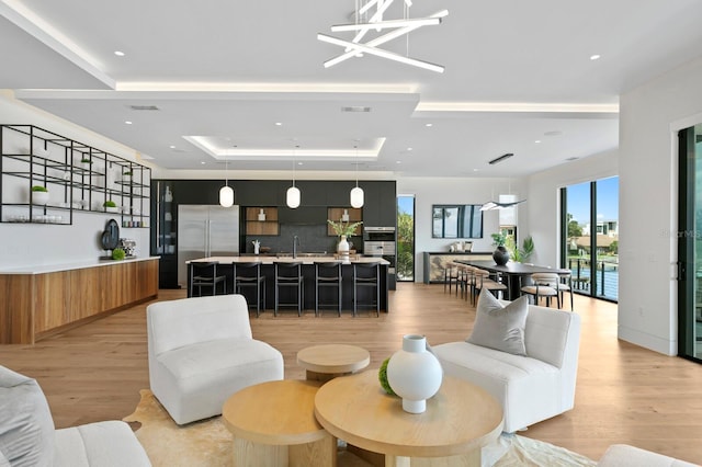 living room featuring a tray ceiling, light hardwood / wood-style floors, and a notable chandelier