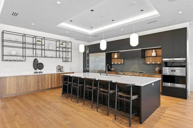 kitchen featuring a large island with sink, a raised ceiling, and hanging light fixtures