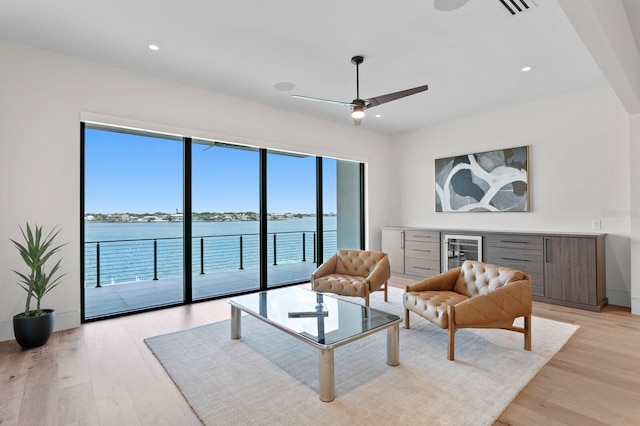 living room with wine cooler, ceiling fan, light hardwood / wood-style flooring, and a water view