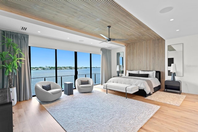 bedroom featuring access to outside, ceiling fan, wooden walls, wood-type flooring, and a water view