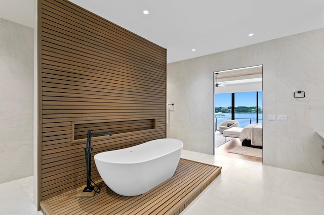 bathroom featuring tile patterned flooring, a water view, tile walls, and a bathing tub