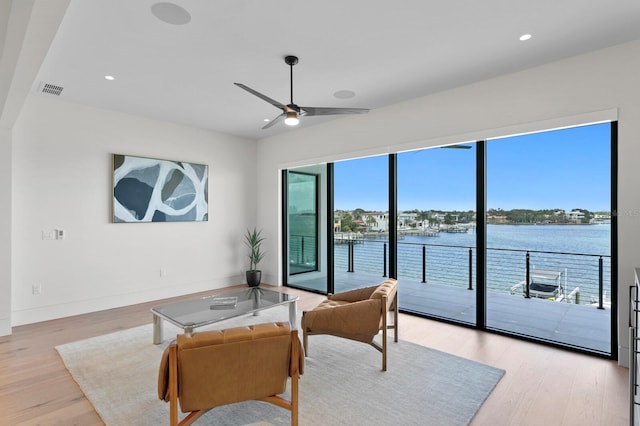 living room with a water view, light hardwood / wood-style flooring, and ceiling fan