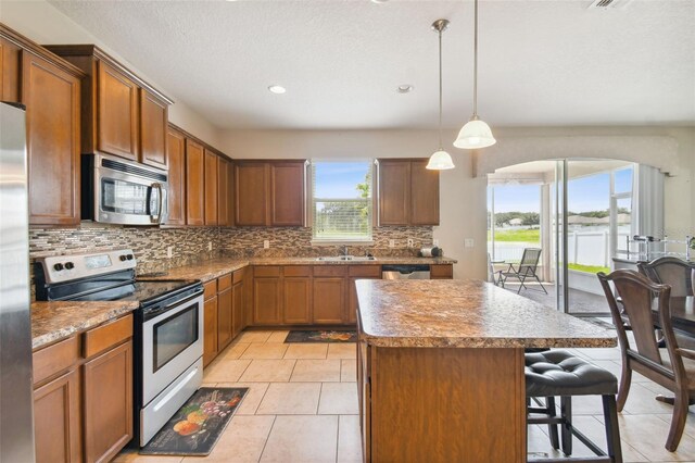 kitchen featuring hanging light fixtures, light tile patterned floors, a kitchen breakfast bar, a kitchen island, and appliances with stainless steel finishes