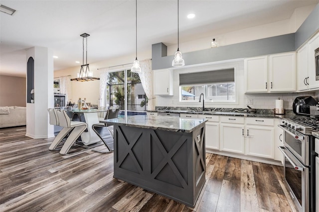 kitchen with decorative light fixtures, range with two ovens, tasteful backsplash, dark hardwood / wood-style flooring, and dark stone countertops