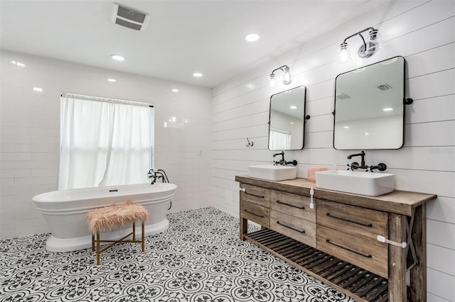 bathroom featuring a tub to relax in, tile patterned flooring, double sink vanity, and tile walls