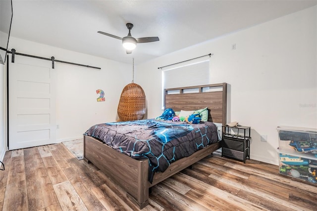 bedroom featuring hardwood / wood-style floors, ceiling fan, and a barn door