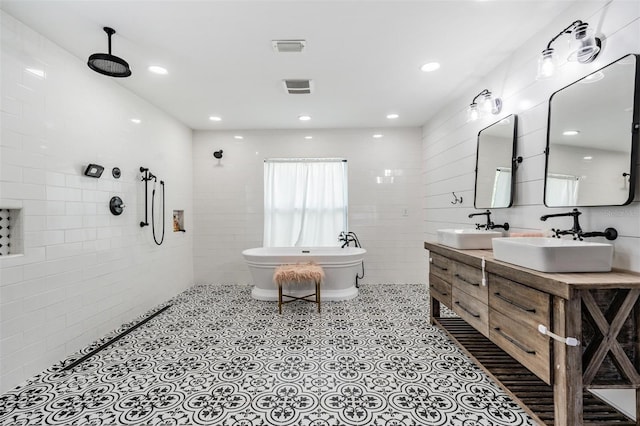 bathroom with tile walls, tile patterned floors, a bathing tub, and dual bowl vanity