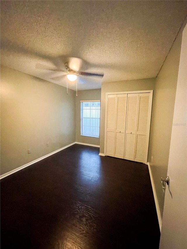 unfurnished bedroom featuring ceiling fan, a textured ceiling, a closet, and dark hardwood / wood-style flooring