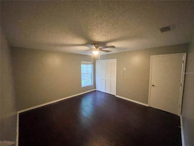 unfurnished bedroom with ceiling fan, a textured ceiling, a closet, and dark hardwood / wood-style flooring