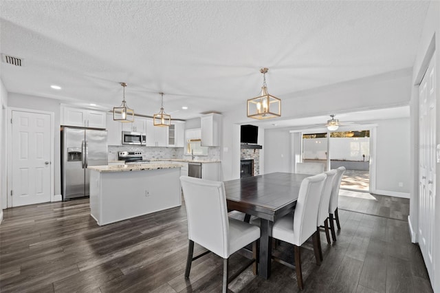 dining area featuring a textured ceiling, ceiling fan, a fireplace, and dark hardwood / wood-style floors