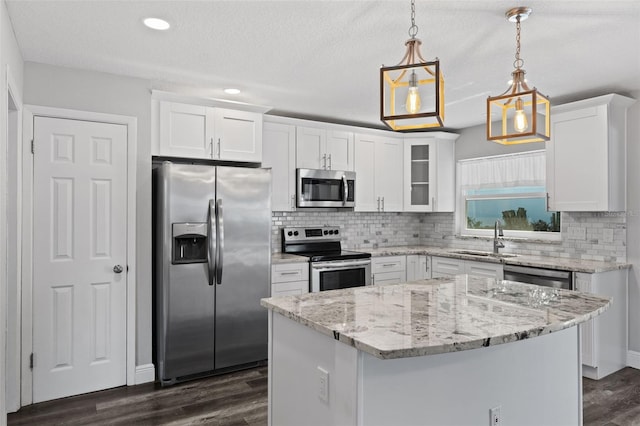 kitchen with a center island, sink, stainless steel appliances, pendant lighting, and white cabinets