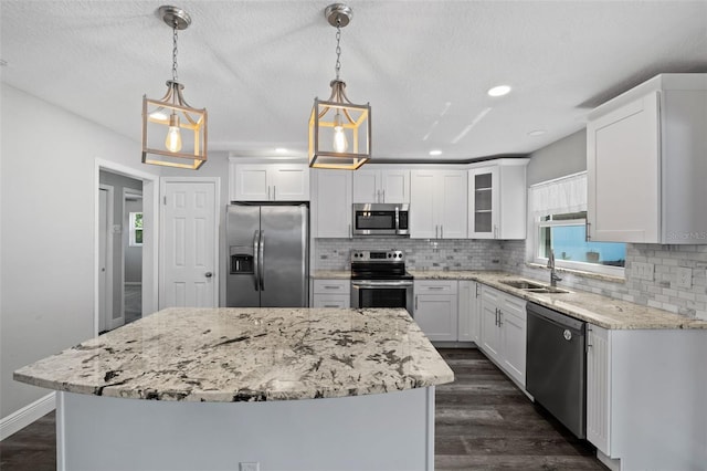 kitchen with appliances with stainless steel finishes, a kitchen island, white cabinetry, and pendant lighting