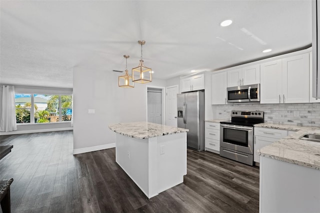 kitchen with light stone countertops, stainless steel appliances, a kitchen island, decorative light fixtures, and white cabinets