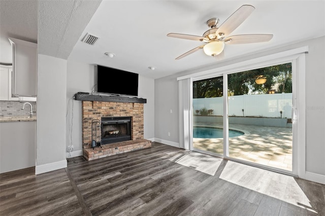 living room featuring ceiling fan, dark hardwood / wood-style flooring, a textured ceiling, and a brick fireplace