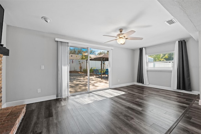 empty room with a textured ceiling, dark hardwood / wood-style flooring, plenty of natural light, and ceiling fan