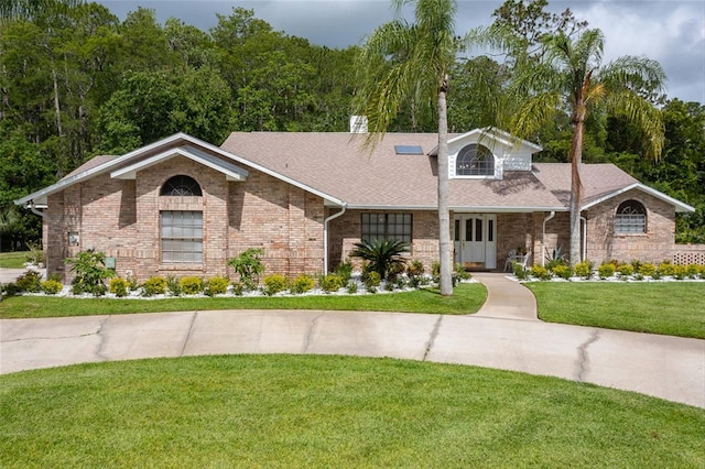 view of front of house featuring brick siding, roof with shingles, and a front yard