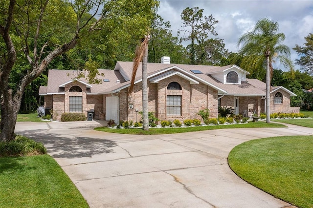 view of front of home with brick siding, curved driveway, and a front lawn