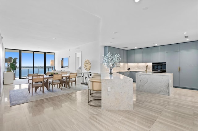 kitchen with oven, a sink, light stone countertops, expansive windows, and backsplash