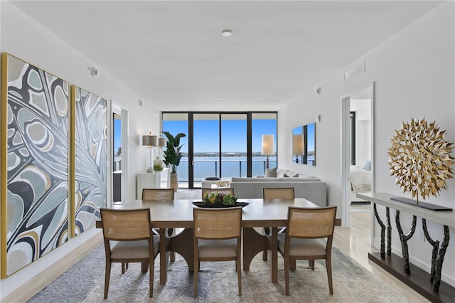 dining space featuring visible vents, a water view, expansive windows, wood finished floors, and baseboards