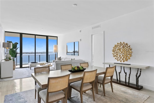 dining space featuring visible vents, a water view, baseboard heating, a wall of windows, and baseboards