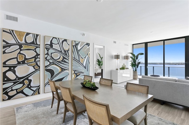 dining space featuring a wall of windows, a water view, wood finished floors, and visible vents