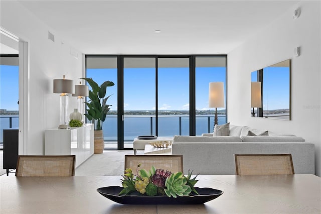 living area featuring a water view, plenty of natural light, visible vents, and a wall of windows