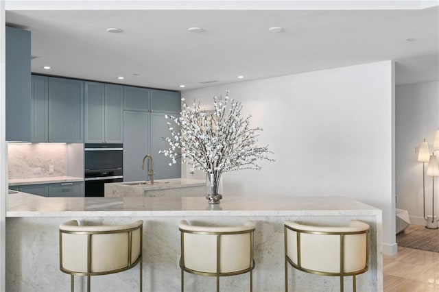 kitchen with recessed lighting, a sink, light wood-type flooring, backsplash, and a kitchen bar