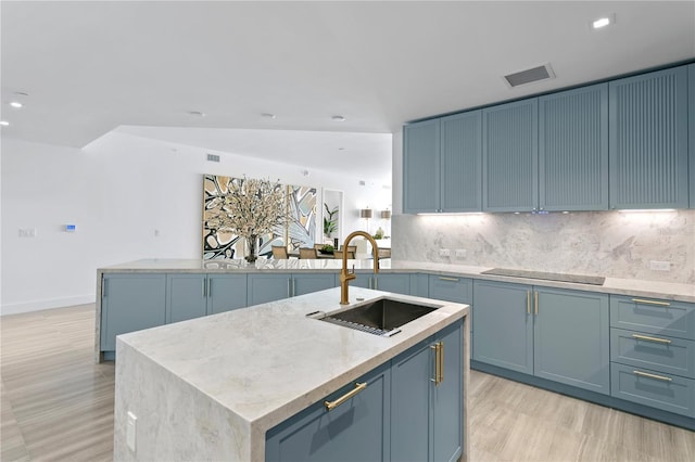 kitchen with black electric cooktop, a sink, visible vents, decorative backsplash, and a center island with sink