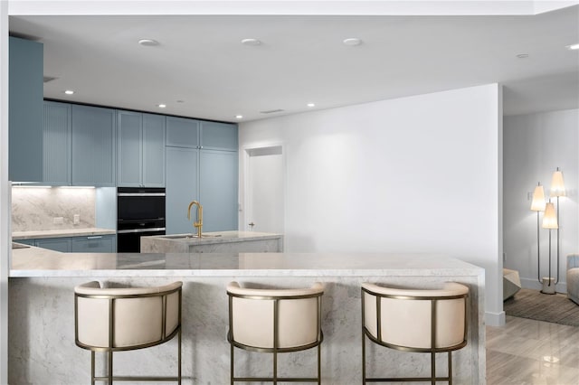 kitchen with light countertops, blue cabinets, a kitchen bar, and dobule oven black