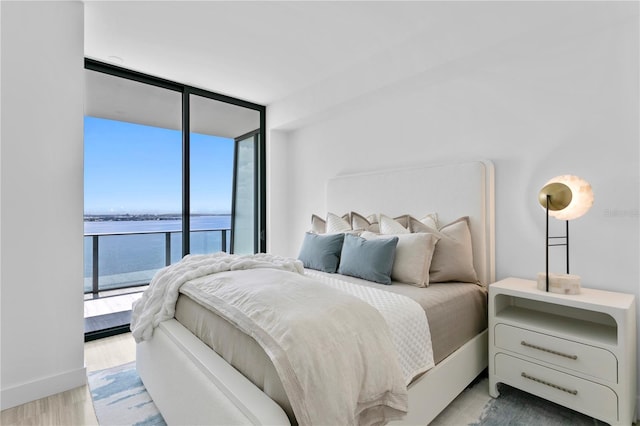 bedroom featuring a water view, baseboards, access to outside, floor to ceiling windows, and light wood finished floors