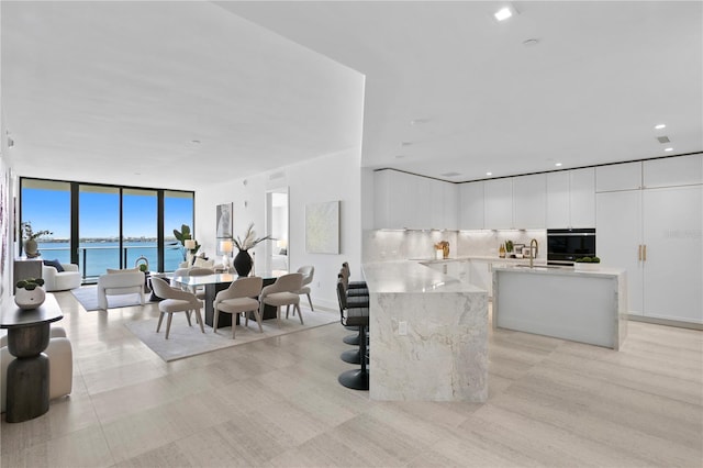 interior space with sink, oven, white cabinetry, a water view, and backsplash