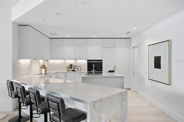 kitchen with a kitchen breakfast bar, light stone countertops, kitchen peninsula, white cabinetry, and tasteful backsplash