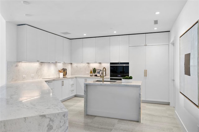 kitchen with black appliances, light stone counters, sink, white cabinetry, and backsplash