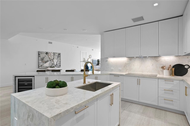 kitchen featuring sink, beverage cooler, white cabinets, and an island with sink