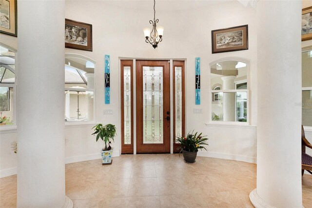 tiled entrance foyer featuring a towering ceiling, ornate columns, and an inviting chandelier