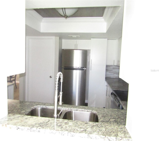 kitchen with white cabinetry, sink, light stone counters, stainless steel fridge, and stove