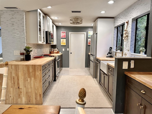 kitchen featuring appliances with stainless steel finishes, butcher block counters, dark brown cabinetry, and decorative backsplash