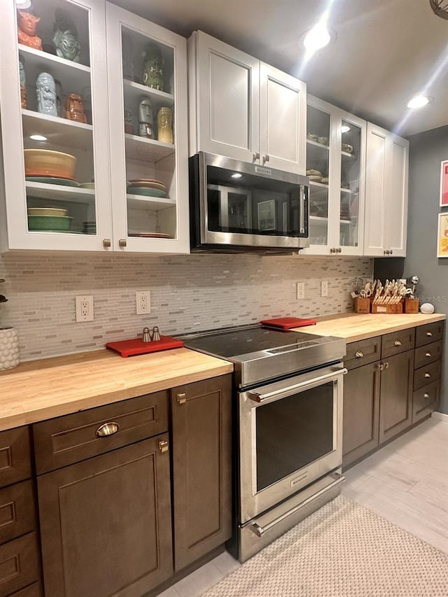 kitchen featuring butcher block counters, dark brown cabinets, stainless steel appliances, white cabinets, and decorative backsplash