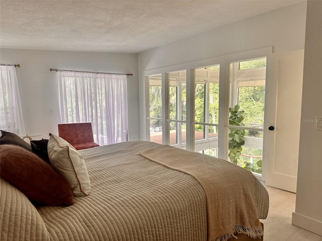 bedroom with multiple windows, light hardwood / wood-style floors, and a textured ceiling