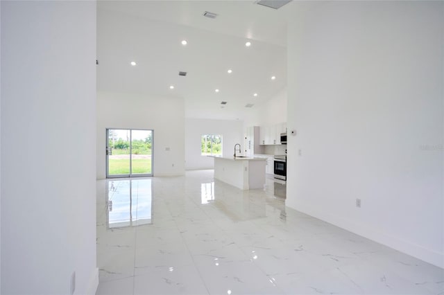 unfurnished living room with baseboards, a towering ceiling, marble finish floor, and a sink