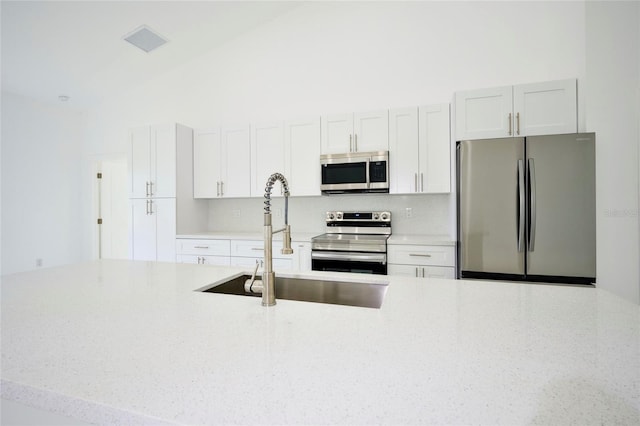 kitchen featuring decorative backsplash, appliances with stainless steel finishes, white cabinets, sink, and a towering ceiling