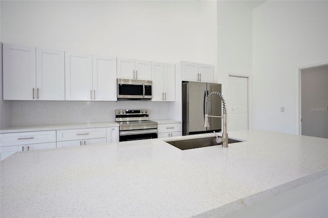 kitchen with tasteful backsplash, stainless steel appliances, sink, white cabinets, and a towering ceiling