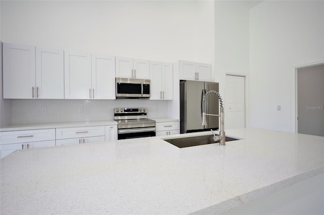 kitchen with a high ceiling, backsplash, light stone countertops, stainless steel appliances, and a sink