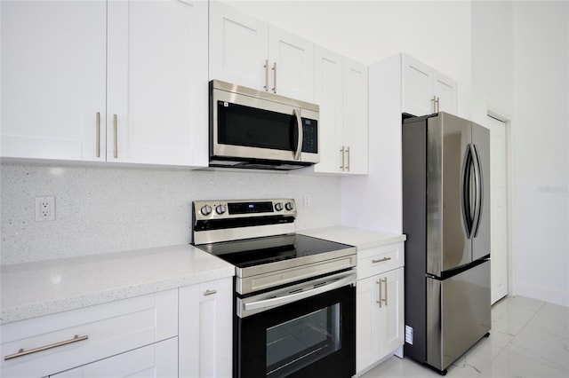 kitchen featuring white cabinets, light stone countertops, decorative backsplash, marble finish floor, and appliances with stainless steel finishes