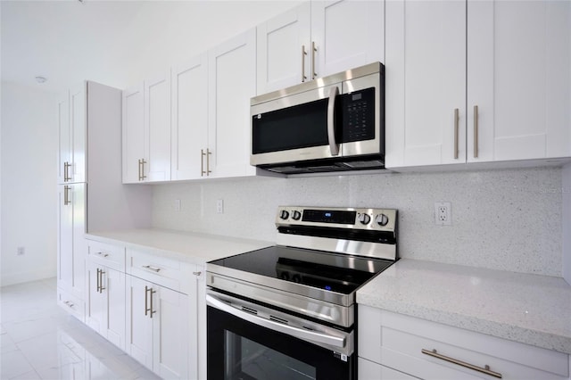 kitchen with stainless steel appliances, white cabinetry, light stone countertops, light tile patterned floors, and tasteful backsplash