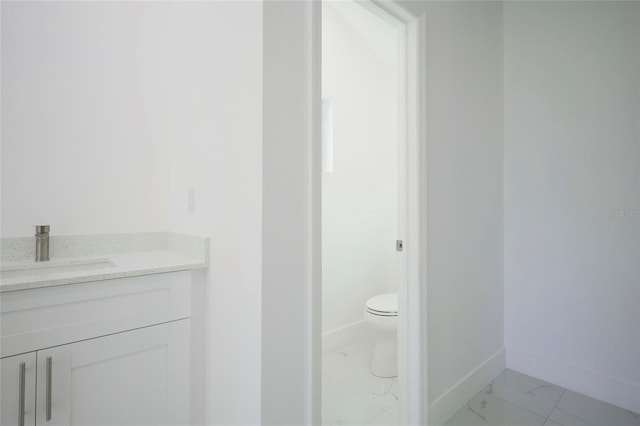 bathroom featuring toilet, marble finish floor, baseboards, and vanity